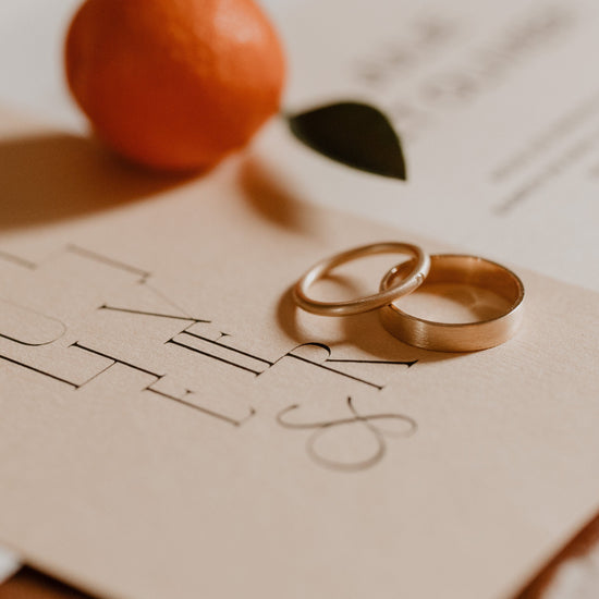 Two wedding rings on a piece of paper with 'I Do' written on it, accompanied by an orange and leaf.
