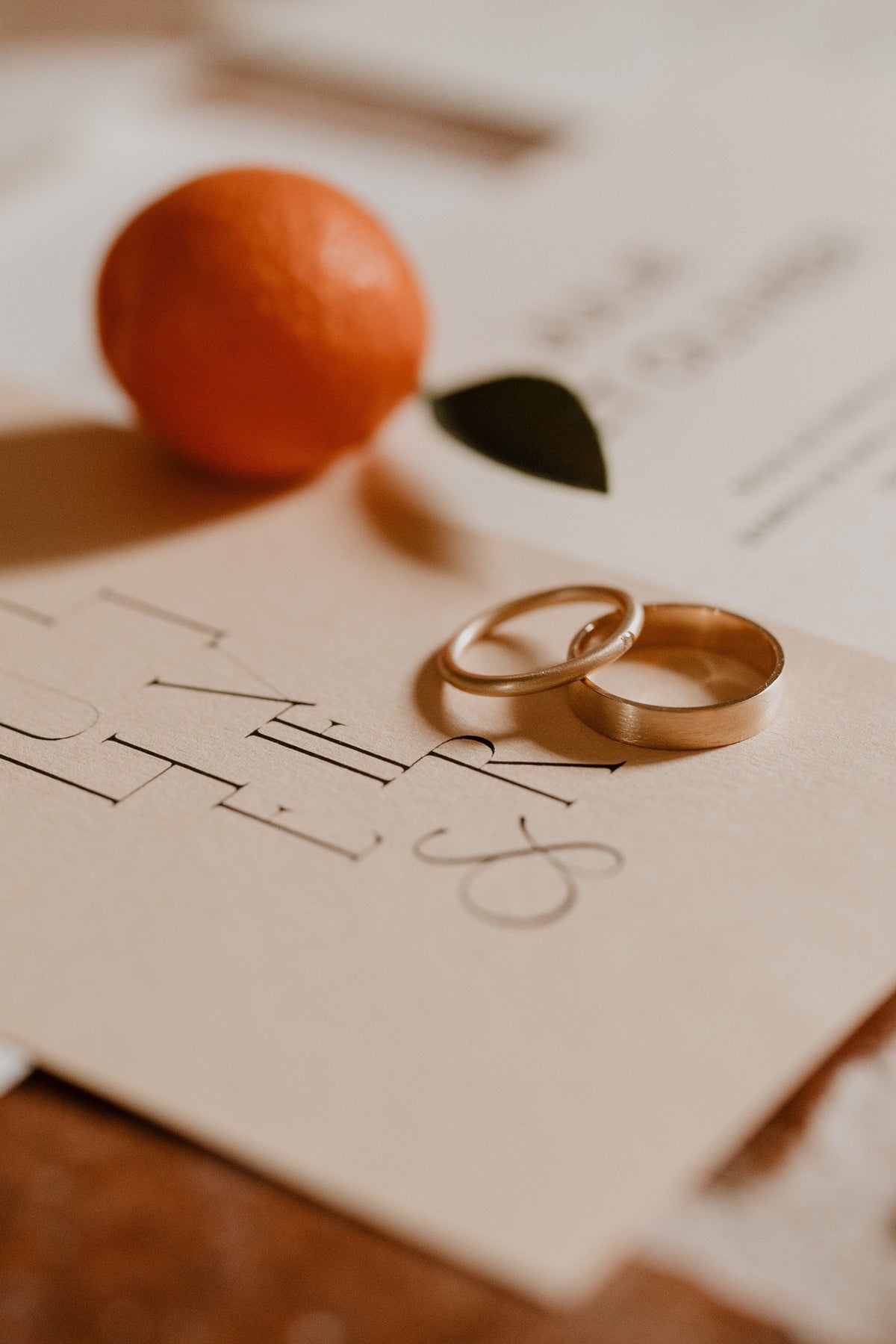 Two wedding rings on a piece of paper with 'I Do' written on it, accompanied by an orange and leaf.