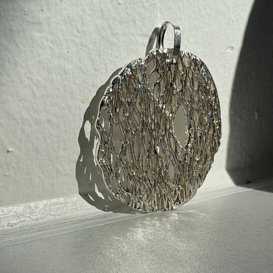 Silver textured pendant on a white surface with a shadow