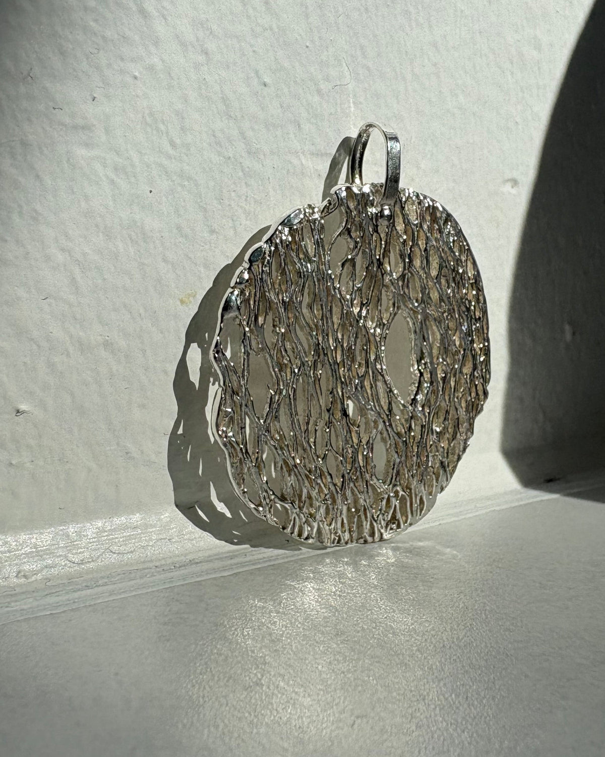 Silver textured pendant on a white surface with a shadow