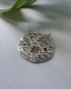 Silver textured pendant with embedded stones on a light gray background
