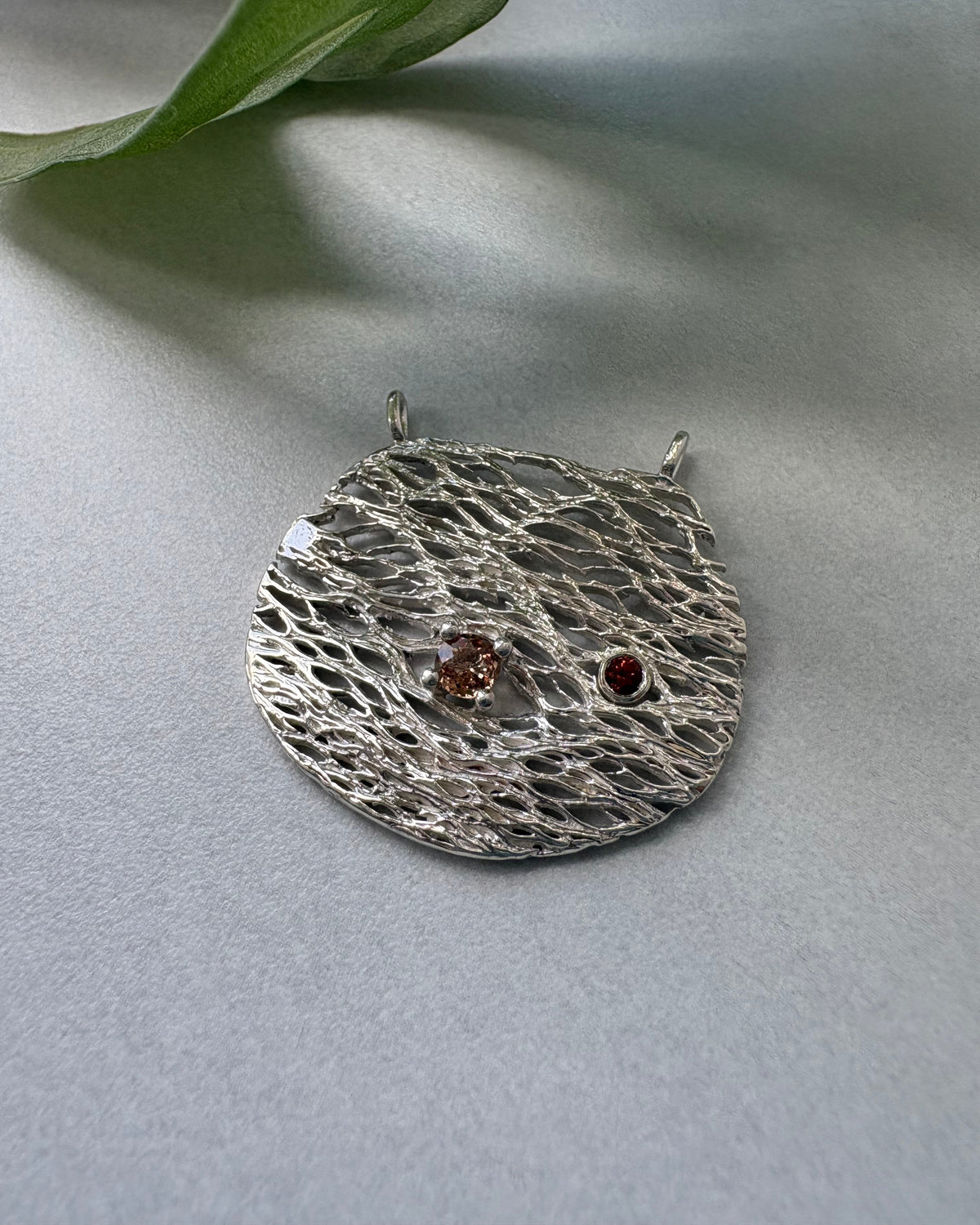 Silver textured pendant with embedded stones on a light gray background