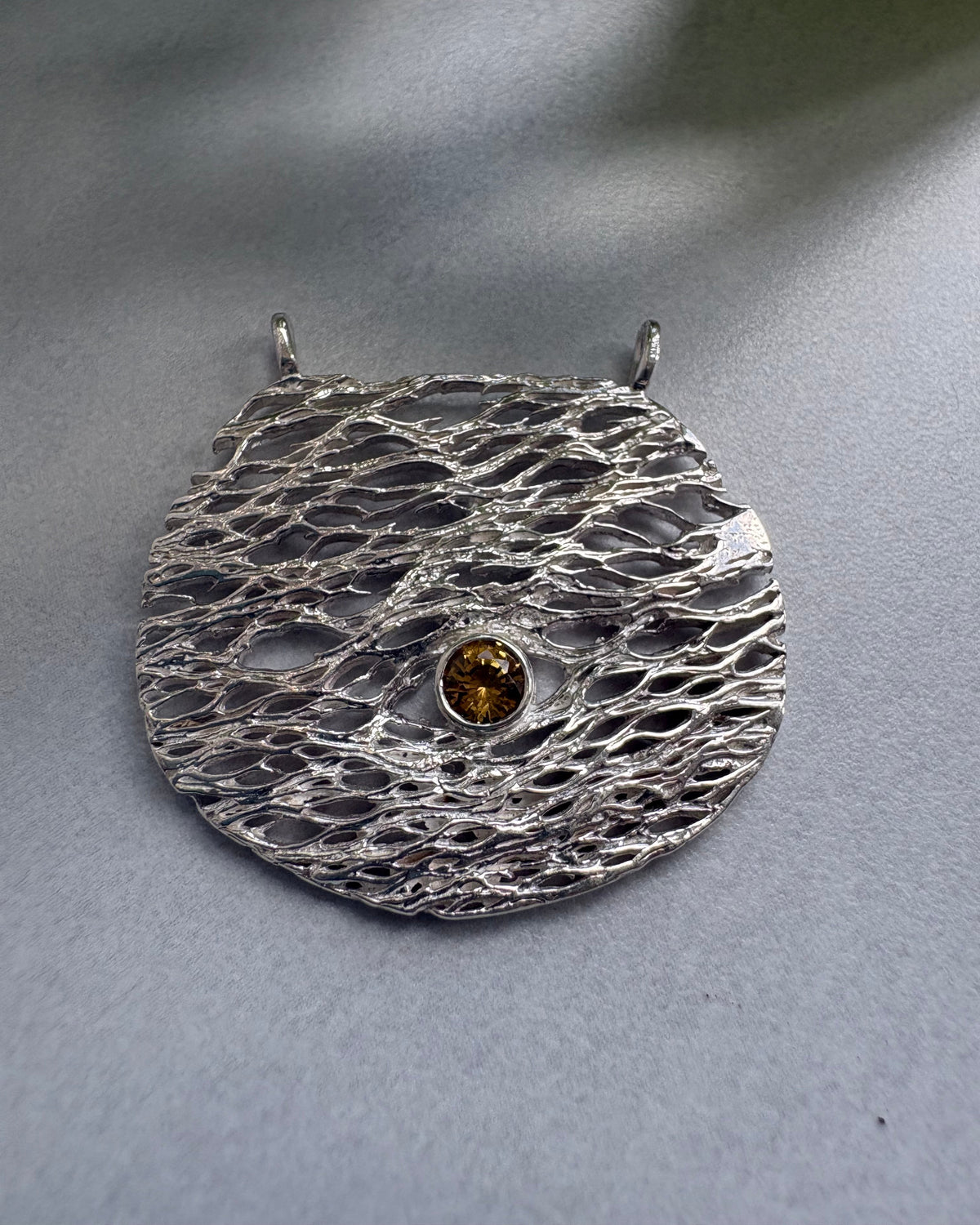 Silver textured brooch with a central gemstone on a gray background