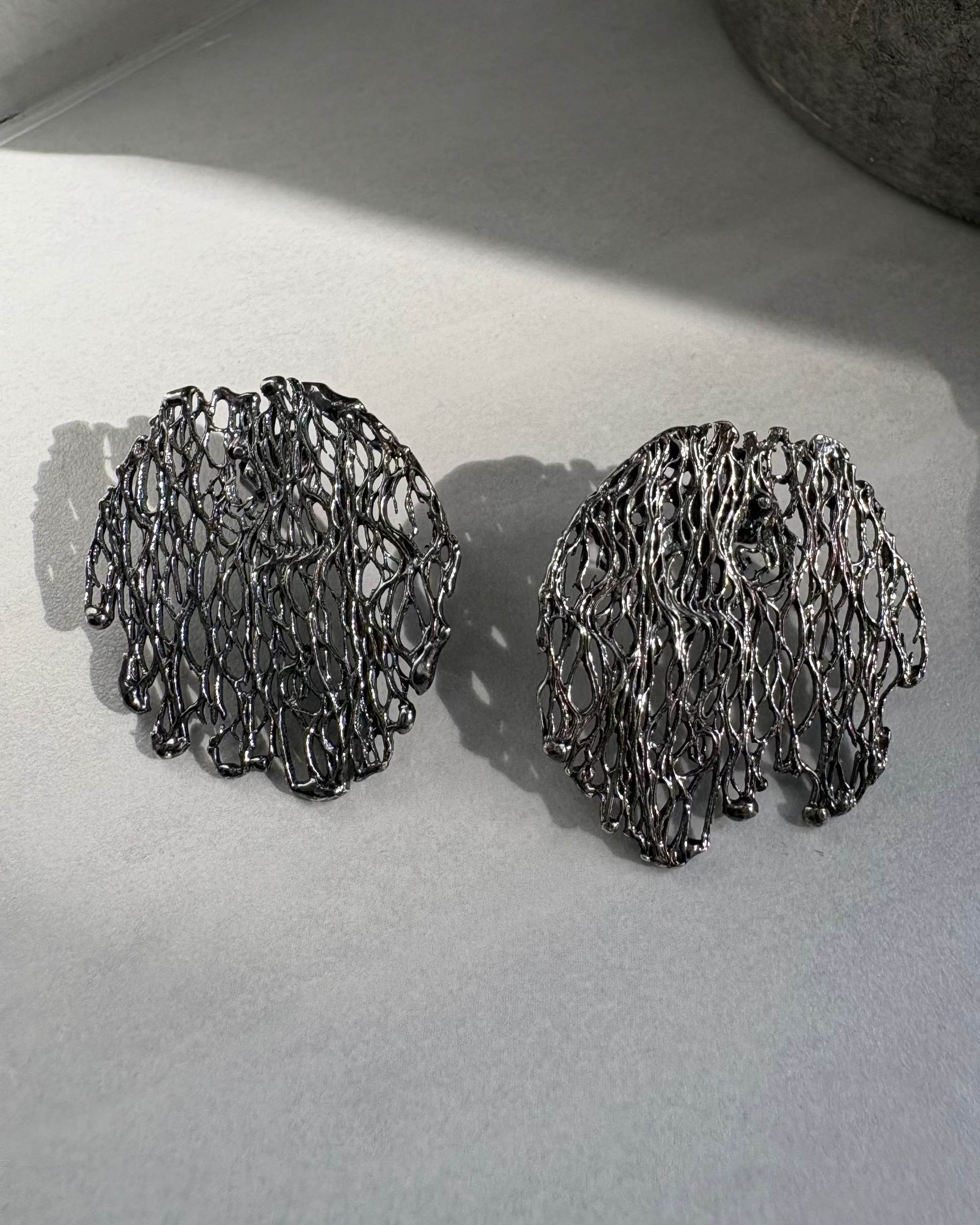 Pair of oxidised silver organic earrings on a light gray surface.