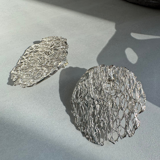 textured Silver earrings on a light gray surface with soft shadows