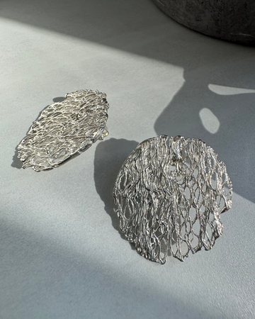 textured Silver earrings on a light gray surface with soft shadows