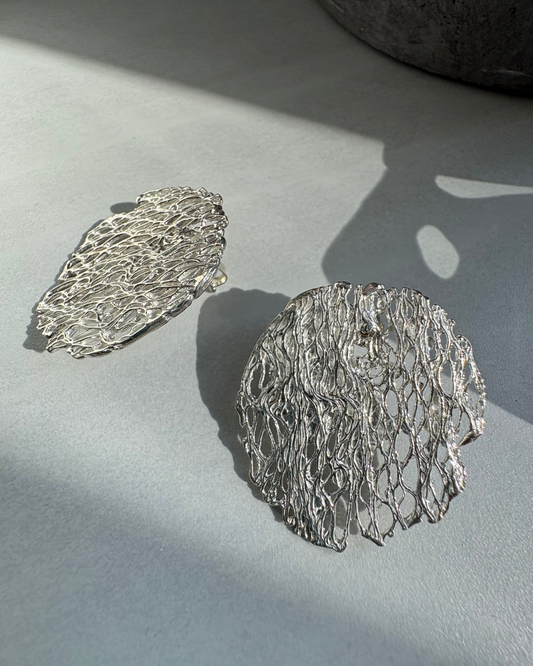 textured Silver earrings on a light gray surface with soft shadows