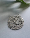 Silver textured round pendant with a white cubic zirconia on a light gray background
