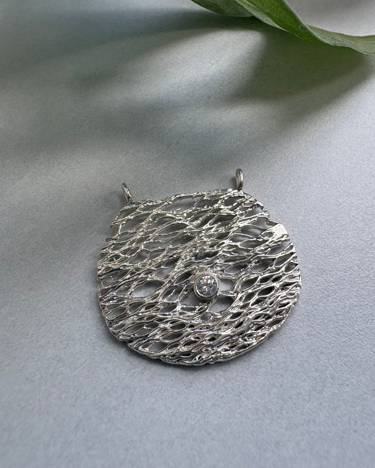 Silver textured round pendant with a white cubic zirconia on a light gray background
