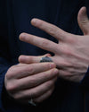A close-up of a person's hands wearing a textured silver ring on their index finger, with a matching silver ring visible on their ring finger, set against a dark navy blue background.