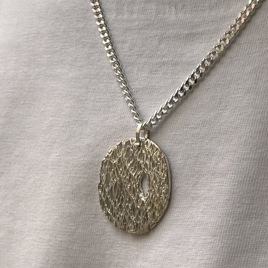 Person wearing a blue patterned sweater and a necklace with a circular pendant.