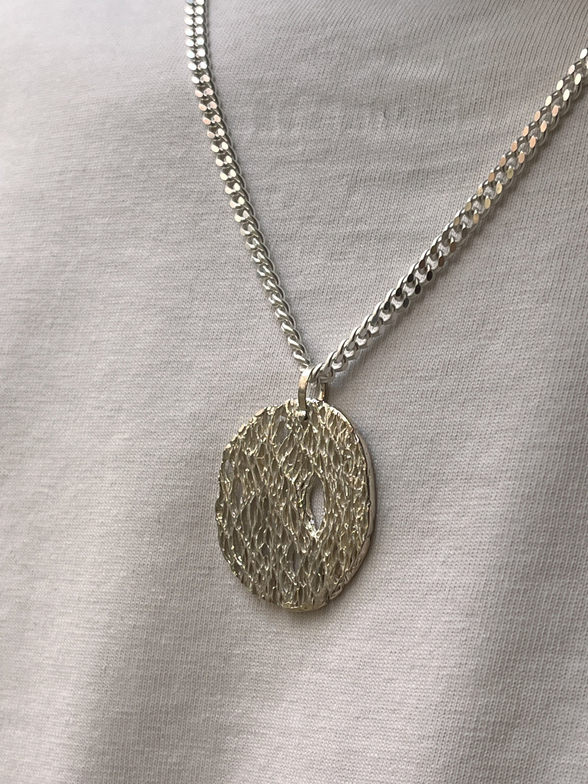 Person wearing a blue patterned sweater and a necklace with a circular pendant.
