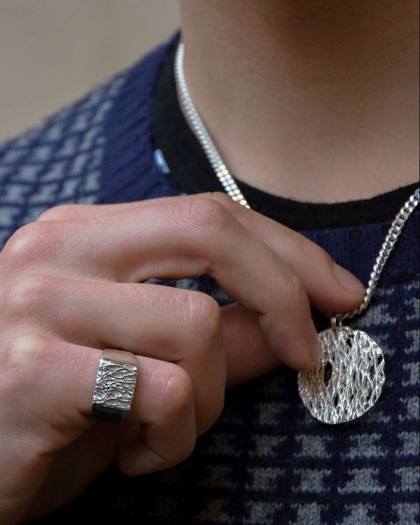 Person wearing a silver ring and necklace with a textured pendant.