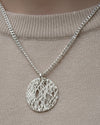 Silver necklace with a textured pendant on a beige background