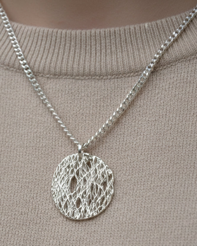 Silver necklace with a textured pendant on a beige background