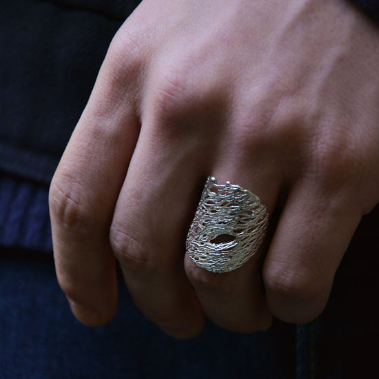 close up a textured chunky silver ring on a model hand with blue jeans