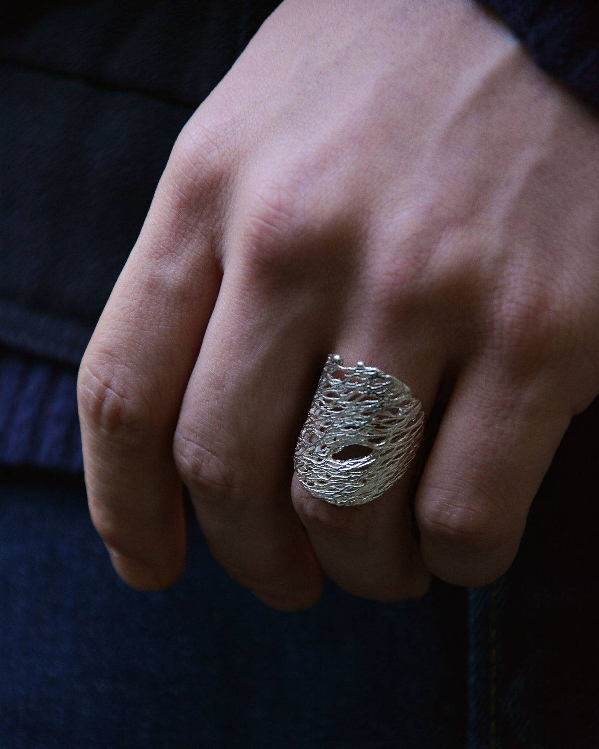 close up a textured chunky silver ring on a model hand with blue jeans