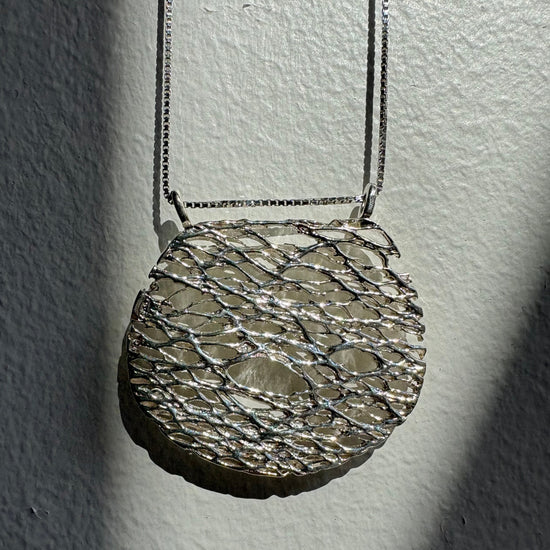 Close-up of a textured silver necklace on a plain background