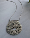 Silver necklace with a textured pendant on a gray background
