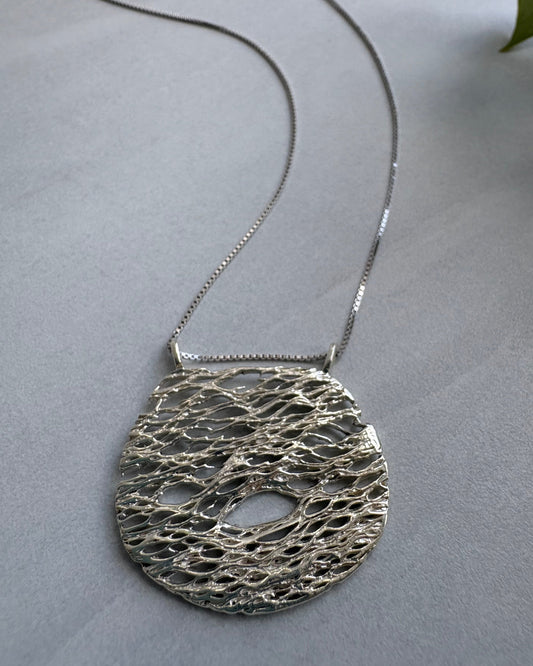 Silver necklace with a textured pendant on a gray background