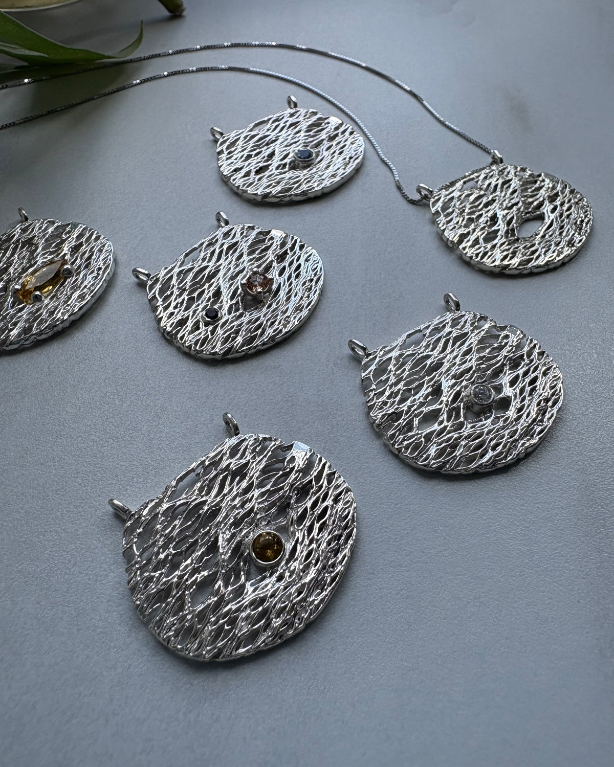 Five textured silver pendats,half moon shaped, with a textured surface and handset stones in different colors