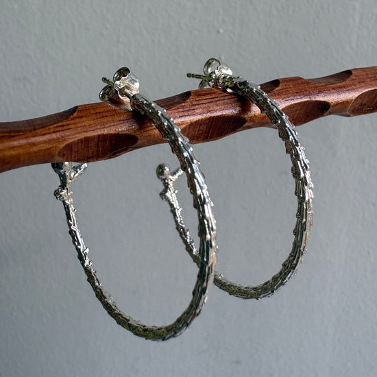 Silver hoop earrings on a wooden stick against a gray background