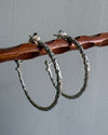 Silver hoop earrings on a wooden stick against a gray background