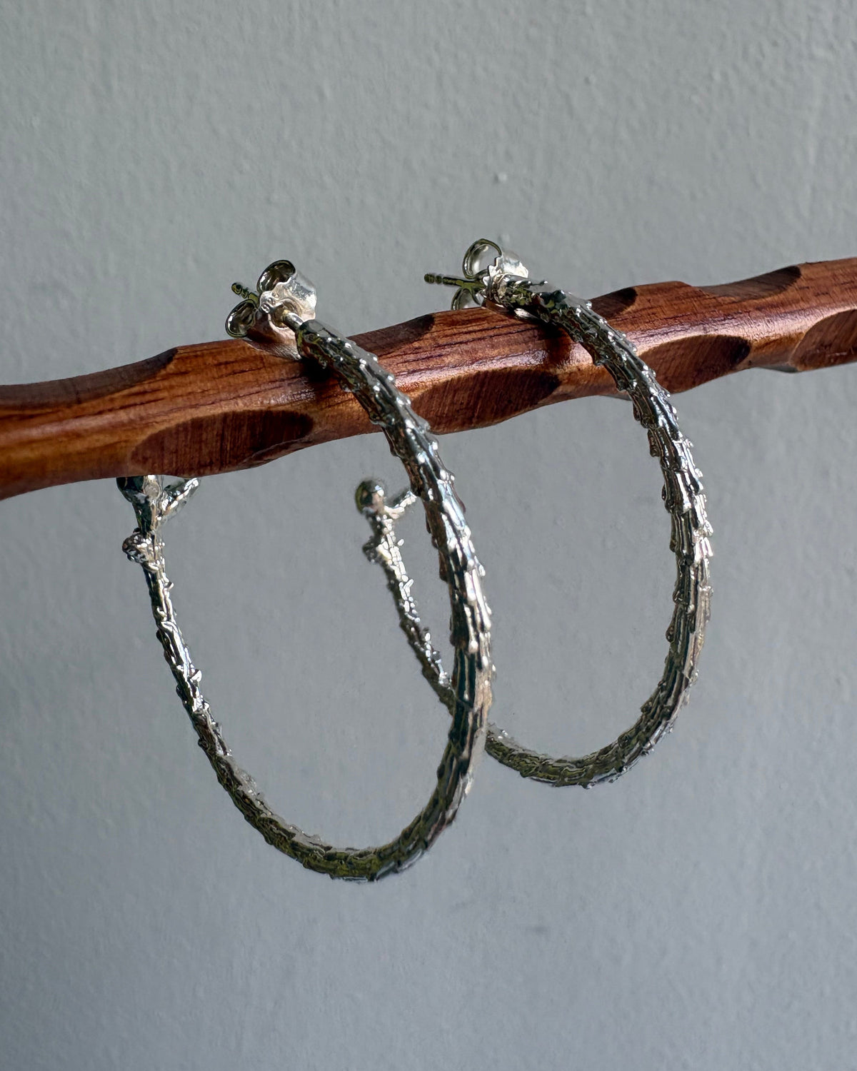 Silver hoop earrings on a wooden stick against a gray background