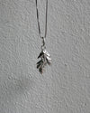 Silver necklace with a leaf-shaped pendant on a gray surface