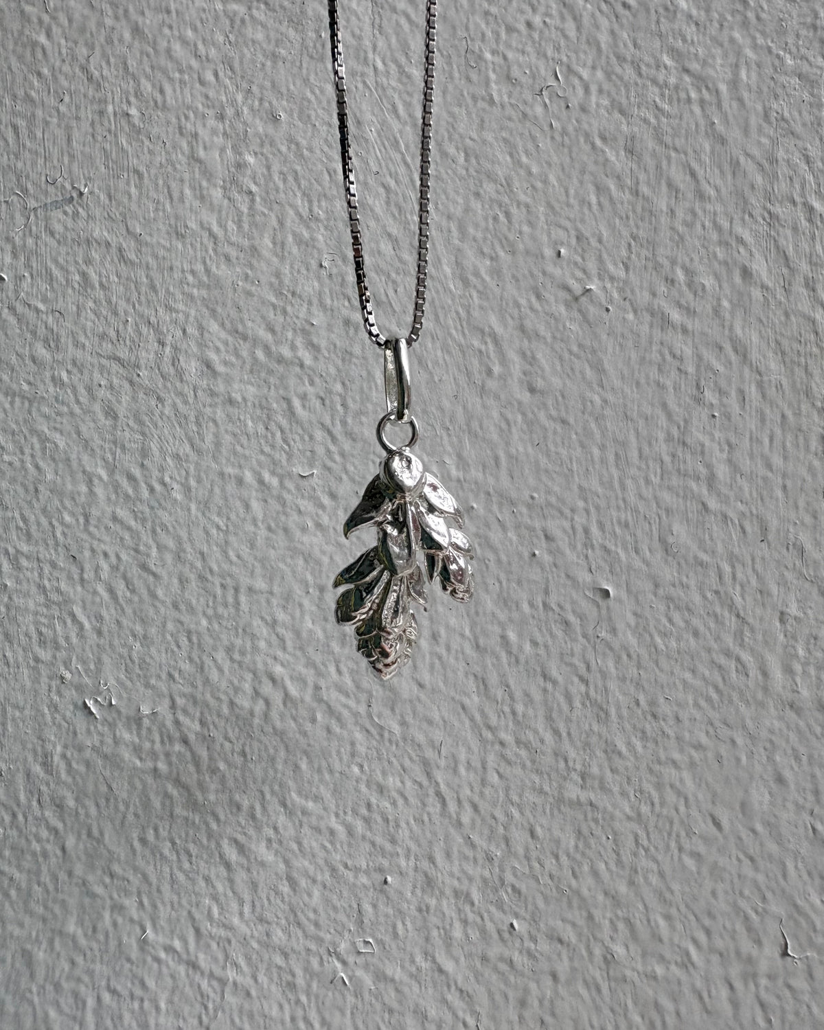Silver necklace with a leaf-shaped pendant on a gray surface