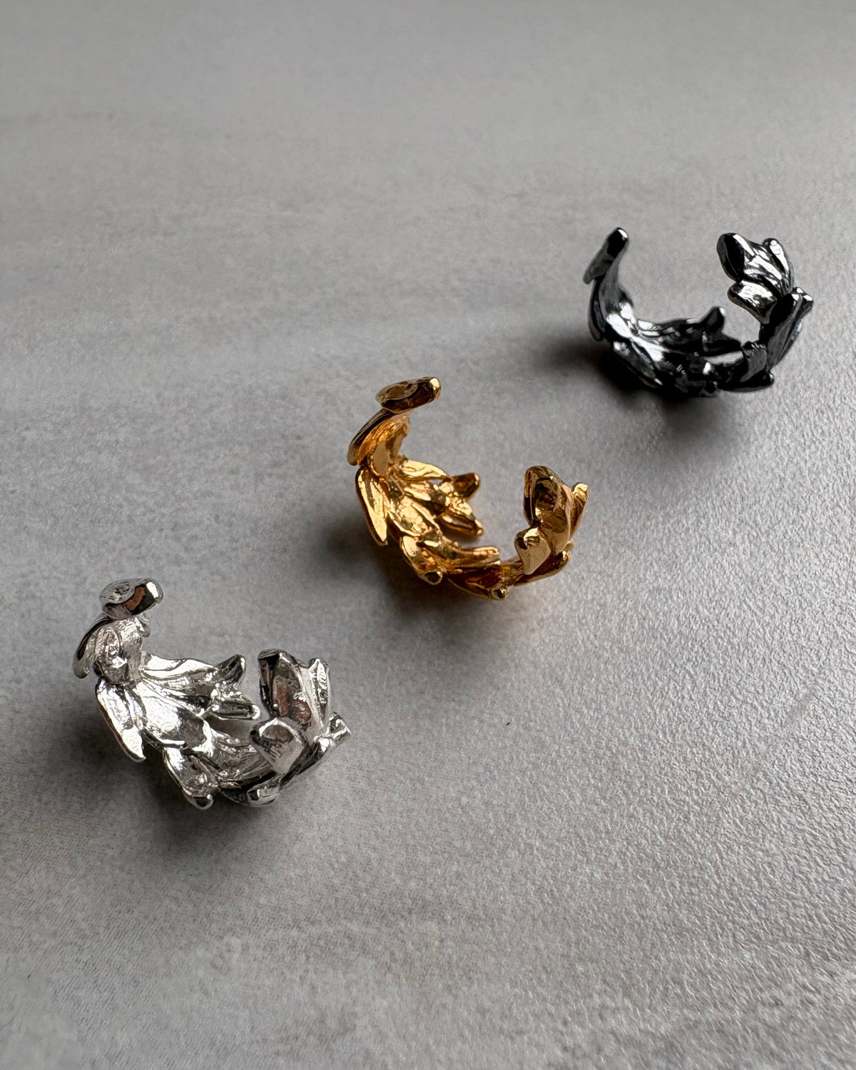 Three silver leaf shaped ear cuff  earrings on a gray surface