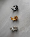 Three leaf shaped ear cuff in black, gold, and silver on a gray background