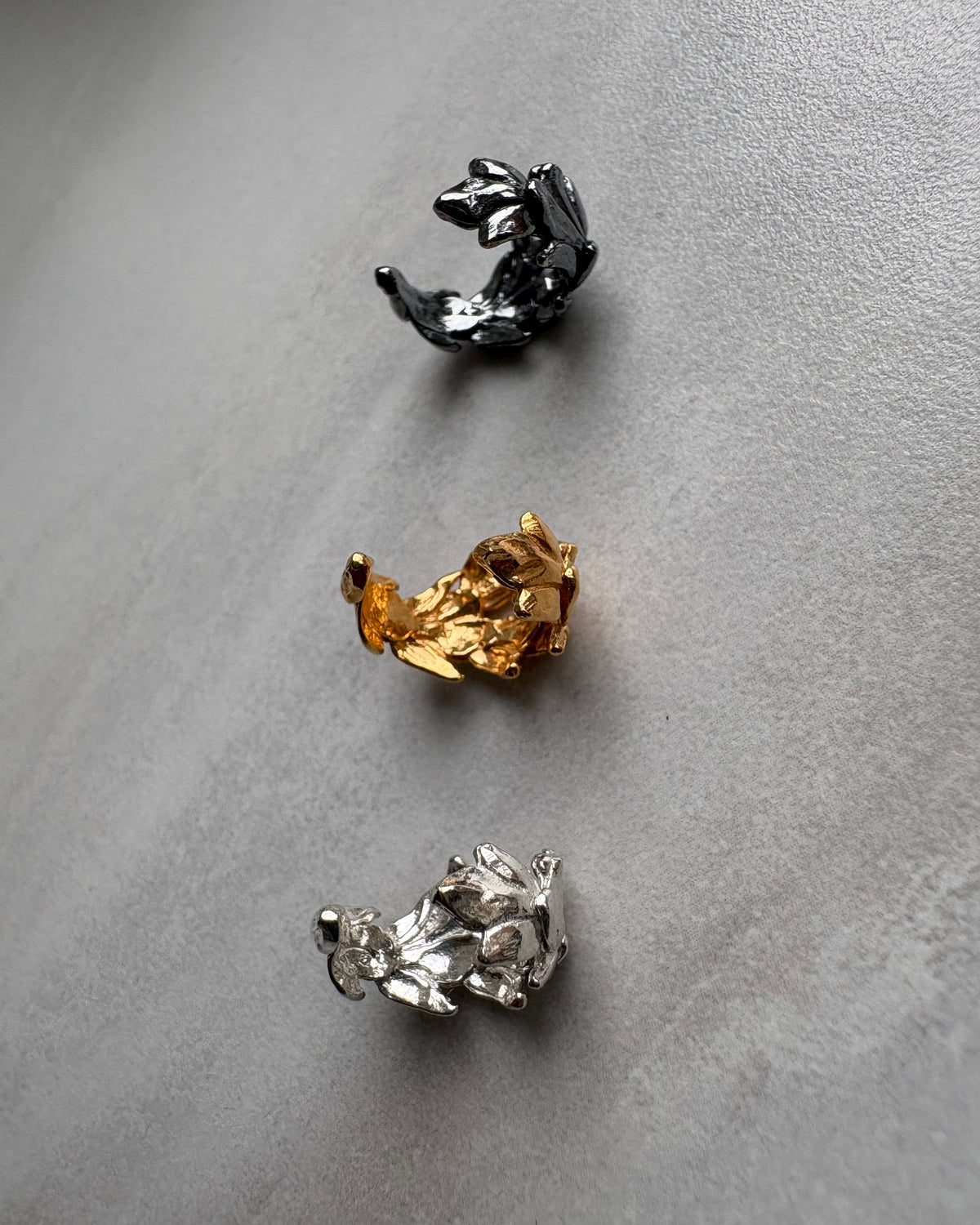 Three leaf shaped ear cuff in black, gold, and silver on a gray background