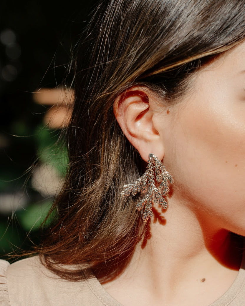 A close-up lifestyle shot of a woman wearing a pair of large, leaf shaped statement earrings.