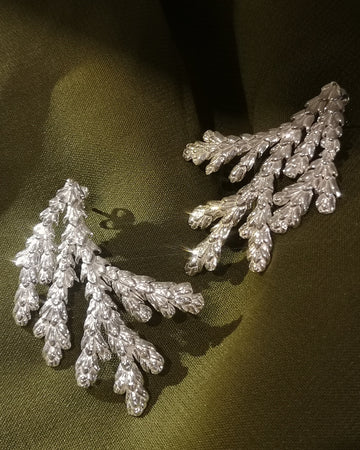 A pair of sterling silver leaf-shaped earrings displayed on a dark olive green fabric background.