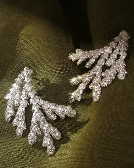 A pair of sterling silver leaf-shaped earrings displayed on a dark olive green fabric background.