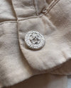 A close-up of a beige linen fabric with a round silver cufflink resting on a light surface.