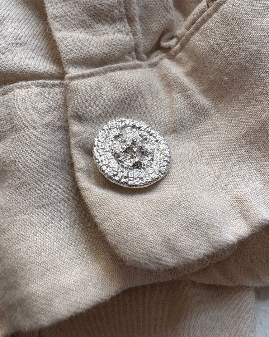 A close-up of a beige linen fabric with a round silver cufflink resting on a light surface.