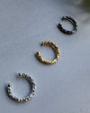 Three ear cuff earrings in black, gold, and silver on a gray surface.