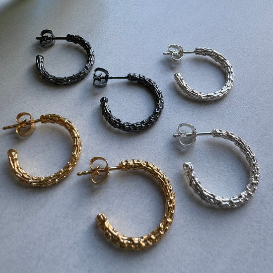 Set of gold, silver, and black hoop earrings on a light gray background