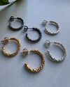 Set of gold, silver, and black hoop earrings on a light gray background