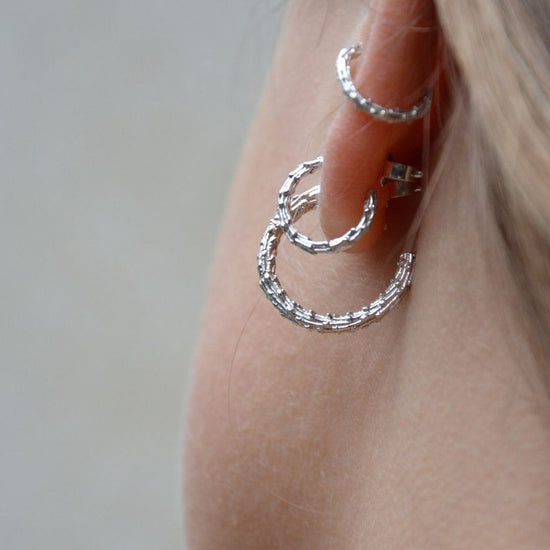 Close-up of a person wearing silver hoop earrings against a neutral background
