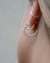 Close-up of a person wearing silver hoop earrings against a neutral background