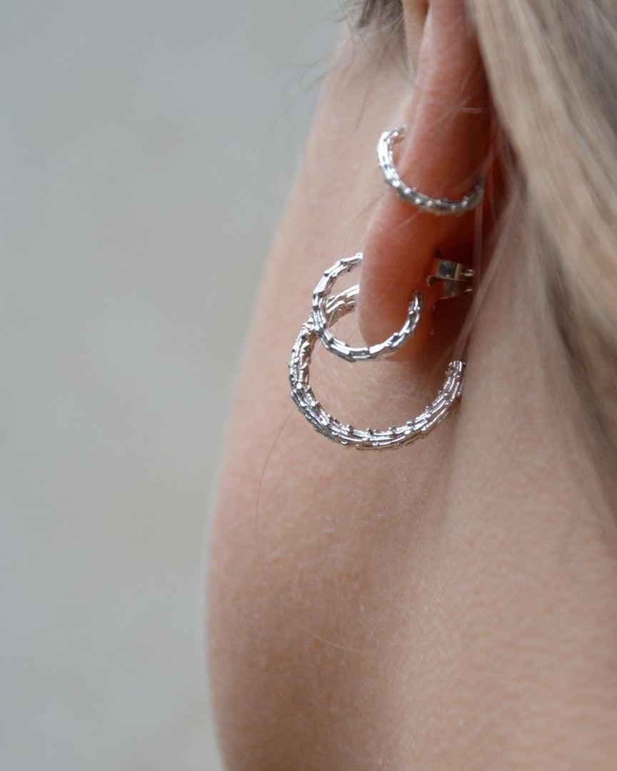 Close-up of a person wearing silver hoop earrings against a neutral background
