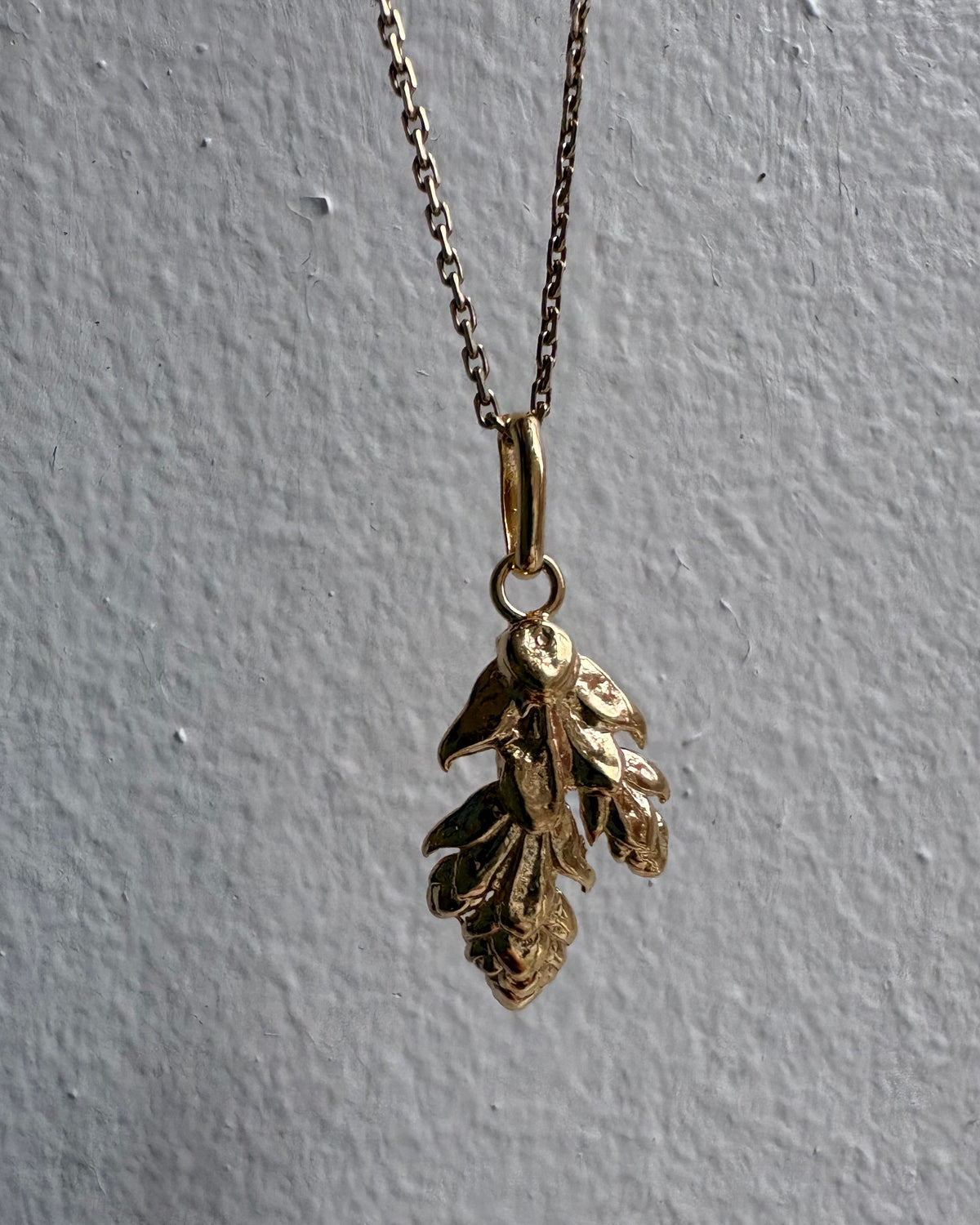 Gold necklace with leaf pendant on a gray background