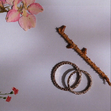 Pair of high-heeled shoes with ribbons, wedding invitations, and rings on a brown surface.
