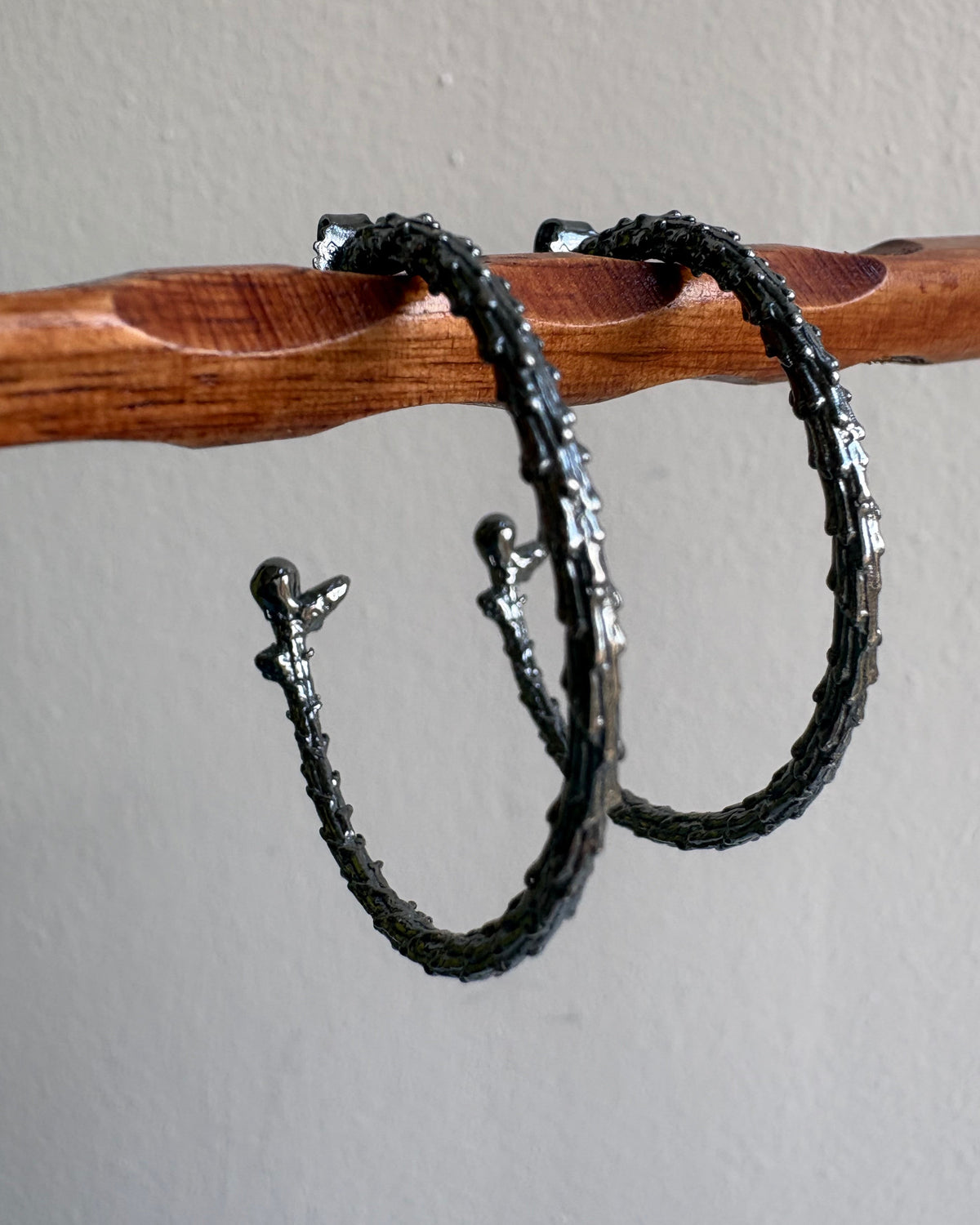 Two oxidised silver earrings on a wooden stick against a gray background