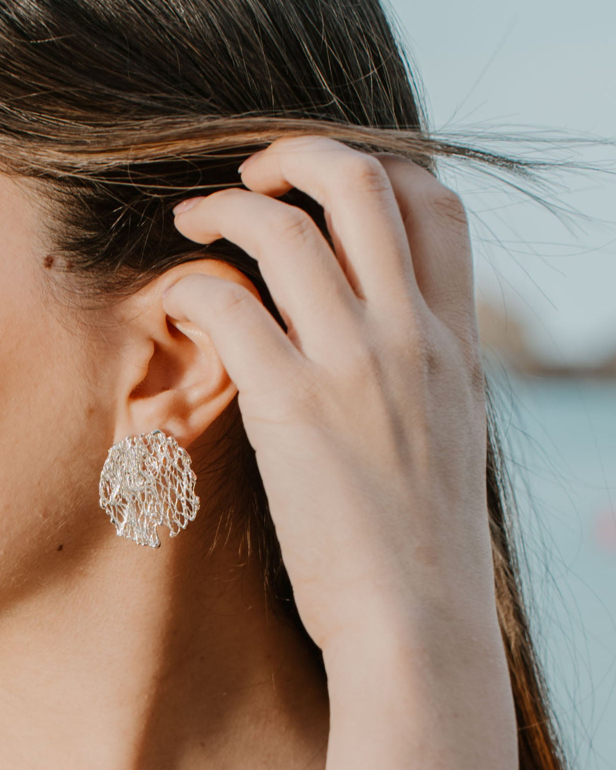 model wearing a textured silver earring on a bright back ground