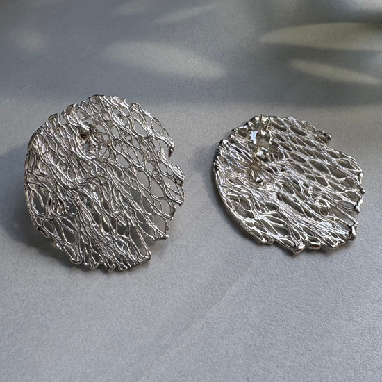 Pair of silver textured round earrings on a gray surface