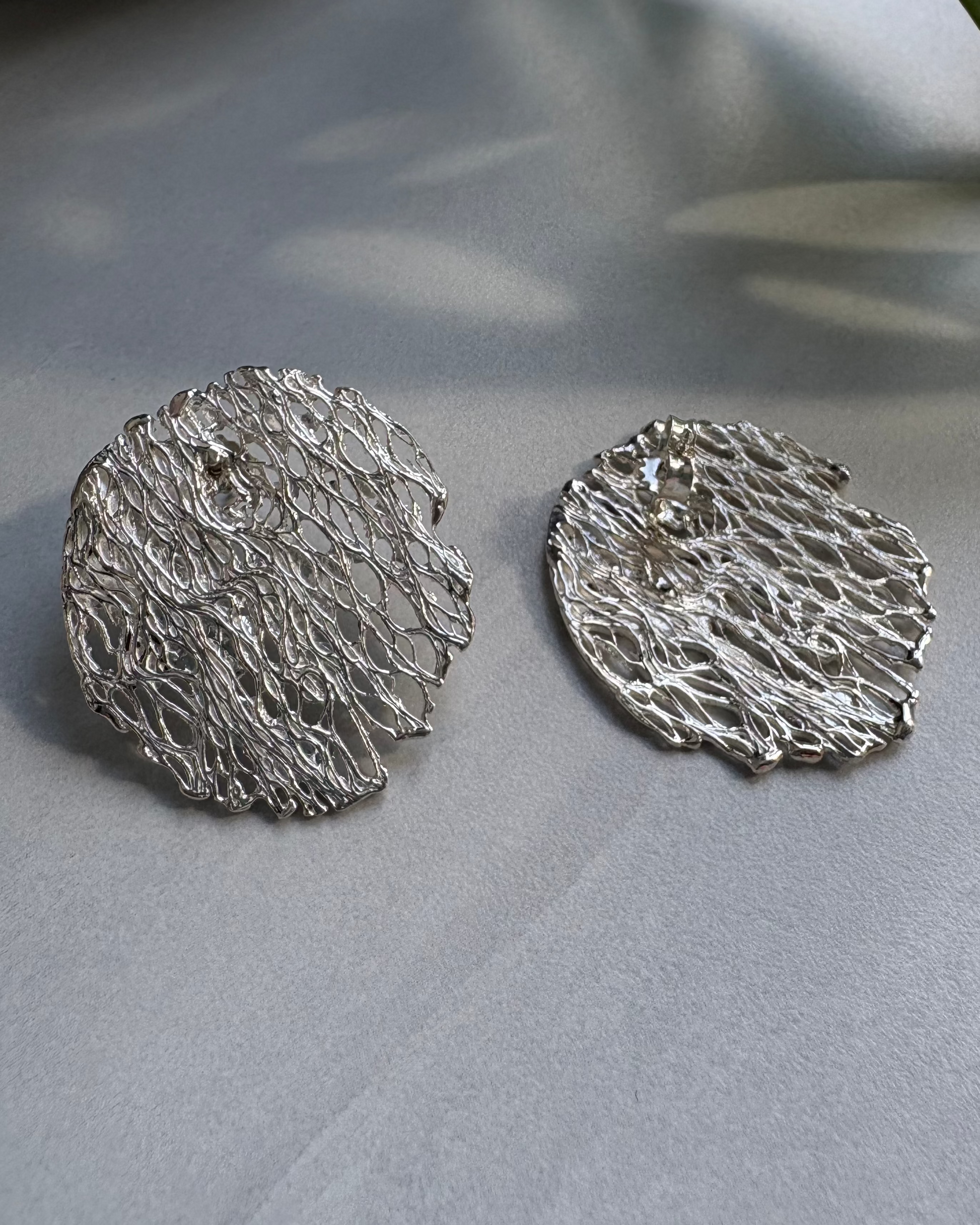 Pair of silver textured round earrings on a gray surface
